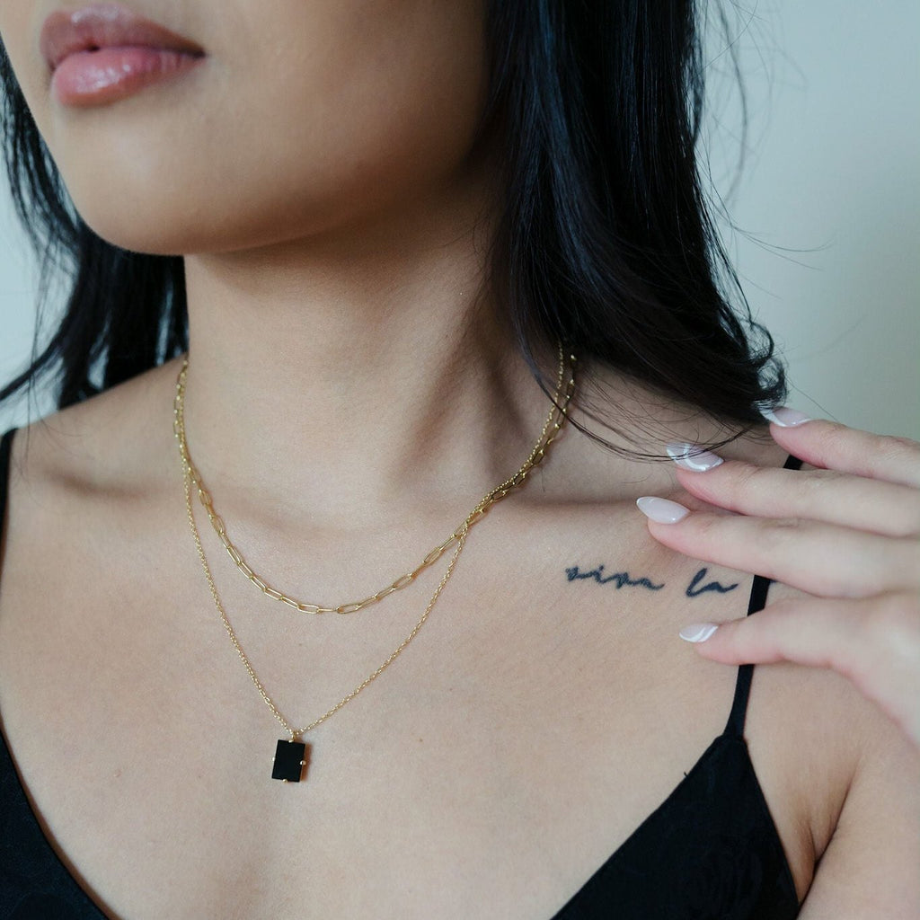 A chic double necklace featuring a paperclip layered design. The first layer is a 16-inch sterling silver necklace, while the second layer showcases a glamorous black tourmaline pendant with a gold accent.