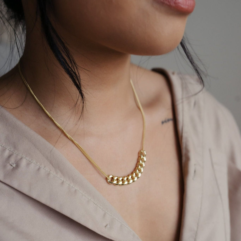 A striking 14K gold necklace with double strands. The center features ten larger link chains intertwined, adding a bold and stylish element. The golden shine and intricate design make it a luxurious accessory