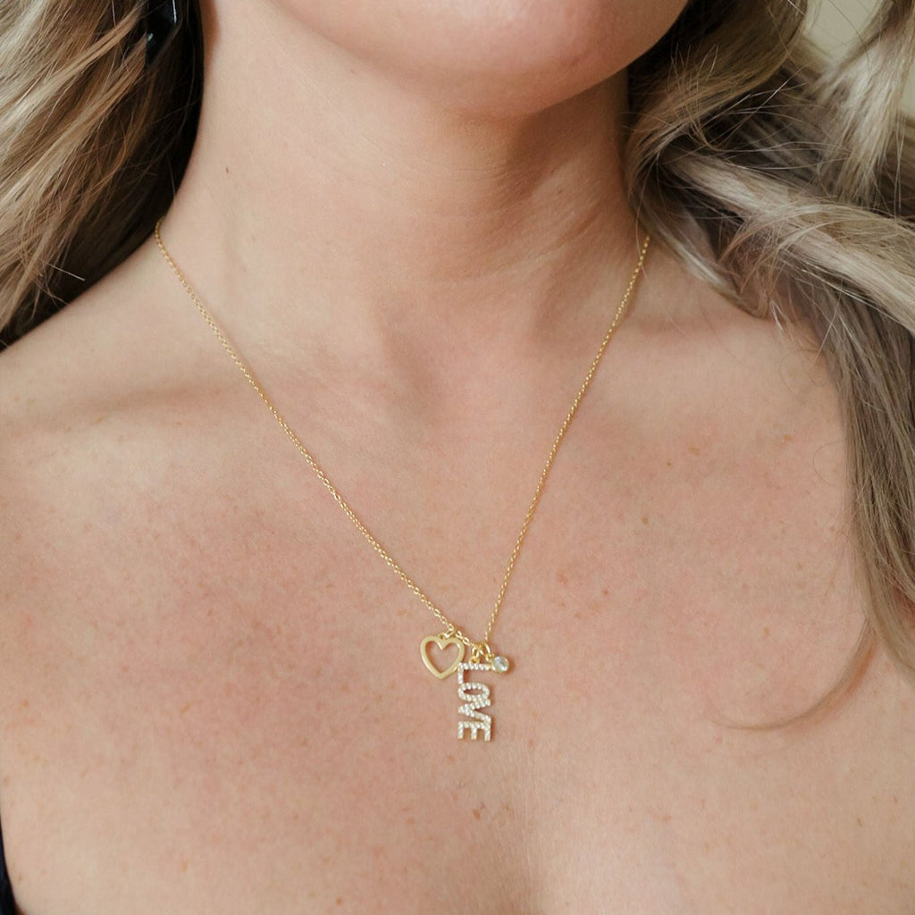 A stunning necklace crafted in 925 sterling silver with 14K gold plating. It features three dainty pendants—a love letter, heart, and round cubic zirconia pendant—creating a charming and elegant accessory