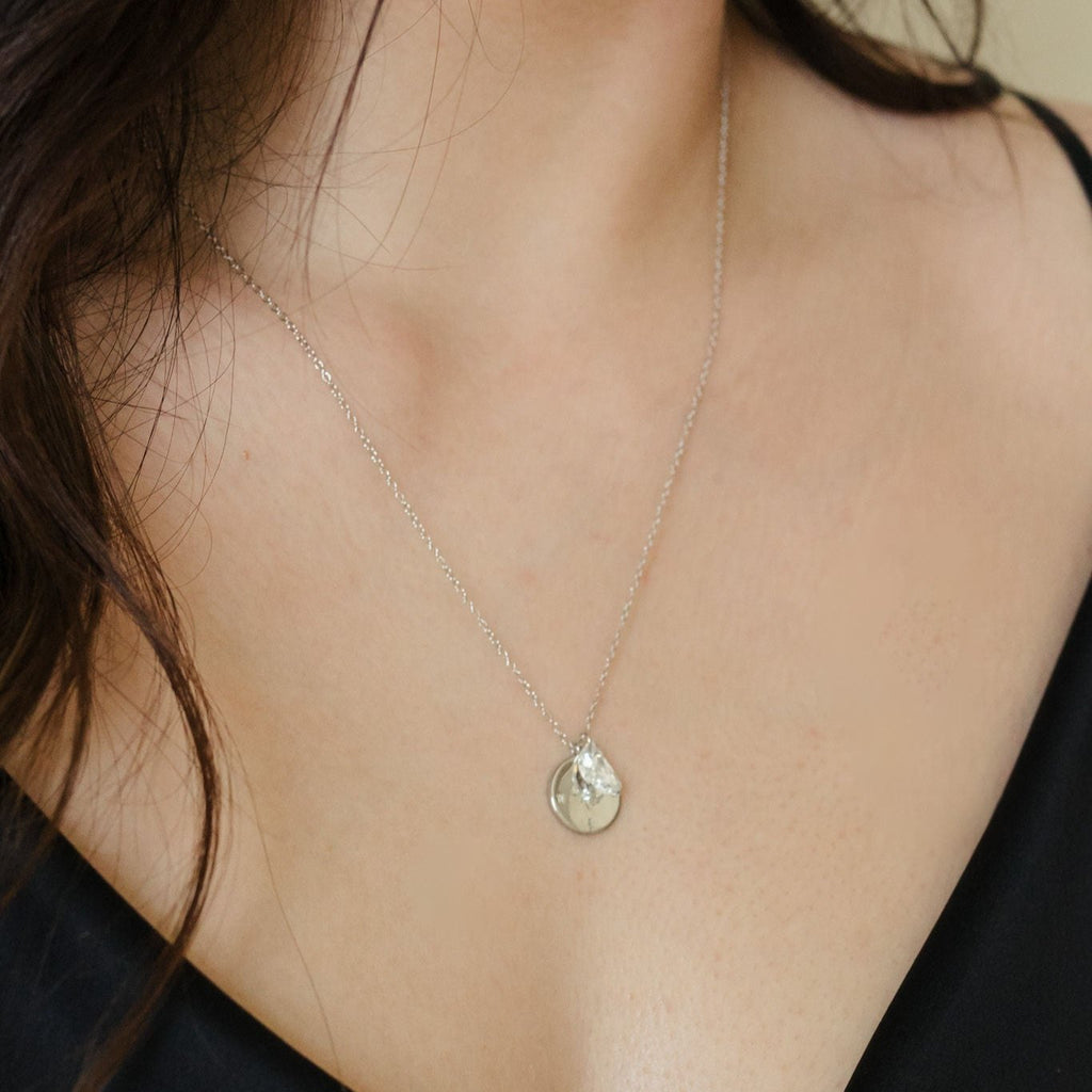 A captivating necklace with a sterling silver compass pendant enhanced by a clear quartz moon shape charm and rhodium plating