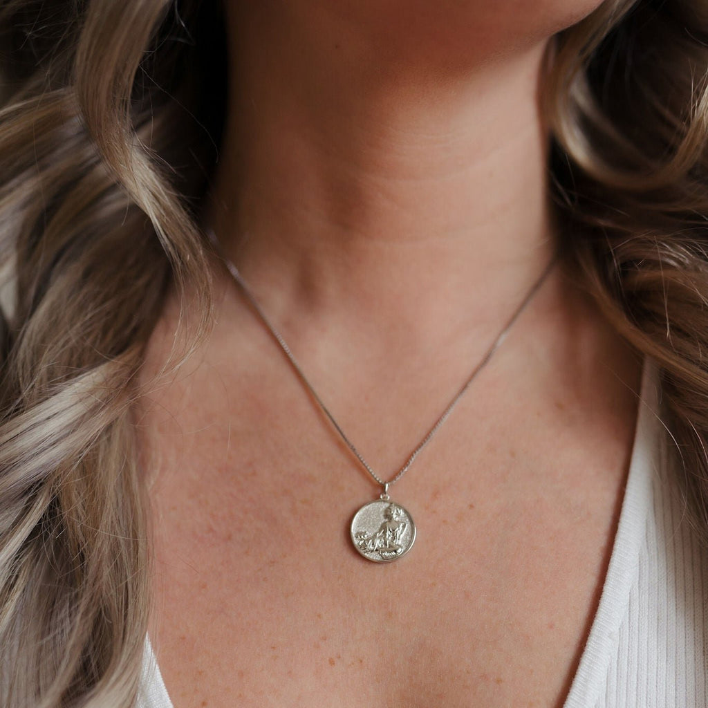 A beautiful sterling silver necklace with a delicate pendant in the shape of a coin, adorned with sparkling gemstones.