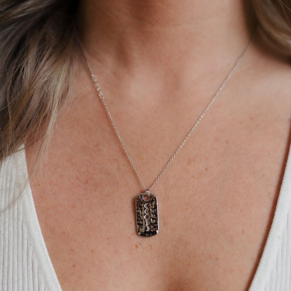 A striking sterling silver necklace with a hammered pendant, beautifully engraved with intricate moon phases. The pendant is adorned with a clear quartz gemstone, suspended on a delicate chain, creating a captivating and celestial-inspired accessory.